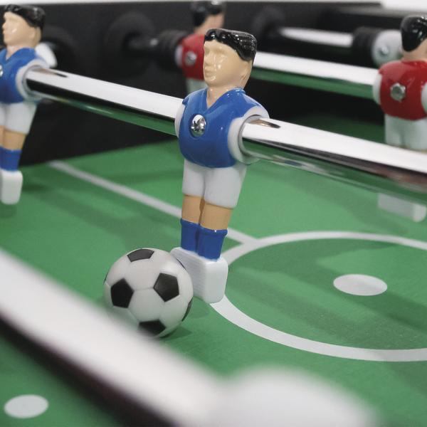 Tischfußball-Spielfigur in blauem Trikot mit Ball auf grünem Spielfeld.