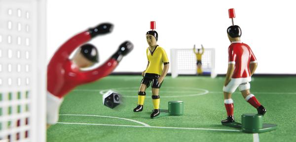 Tischfußballspieler in Aktion, Torwart hält Ball, Spiel auf grünem Spielfeld mit Toren.