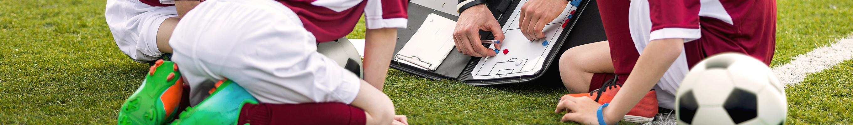 Drei Kinder und ein Trainer in Sportkleidung, die auf einer Wiese sitzen.