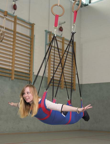 Frau in roter und blauer Schwerkraft-Therapie-Hängematte in Turnhalle mit Holzgeräten.