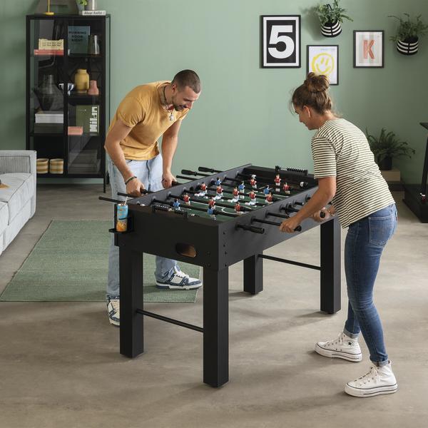 Zwei Personen spielen Tischkicker an einem schwarzen Tischkicker Rapido im Wohnzimmer