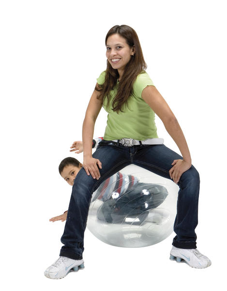 Frau sitzt auf transparentem Ball, Kind schaut spielerisch durch Ball hindurch.