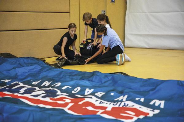 Kinder bereiten in der Turnhalle eine aufblasbare Werbebande vor.