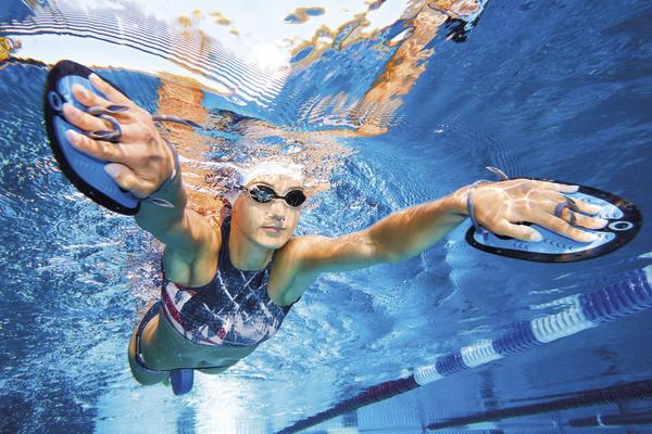 Schwimmerin trainiert mit Handpaddles unter Wasser im Schwimmbecken.