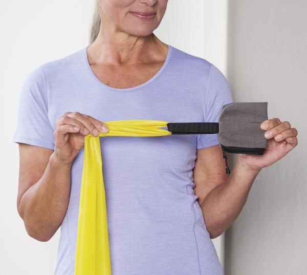 Frau in lila Shirt hält gelbes Widerstandsband mit Griff für Fitnessübungen.