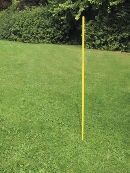 Gelber Slalomstange steht auf grünem Rasen vor dichtem Buschwerk im Garten.