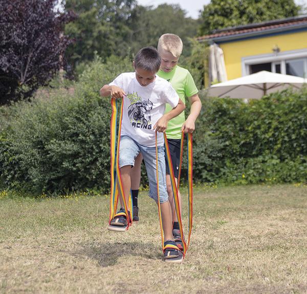 Zwei Jungen spielen im Garten mit bunten Laufbändern an den Füßen.