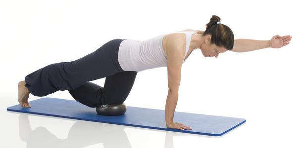 Frau macht Balance-Übung auf Matte mit Ball unter Knie, trainiert Stabilität und Kraft.