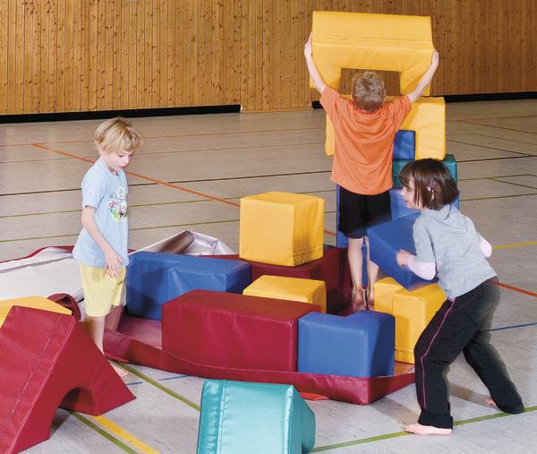 Kinder spielen mit bunten Schaumstoffbausteinen in einer Turnhalle.