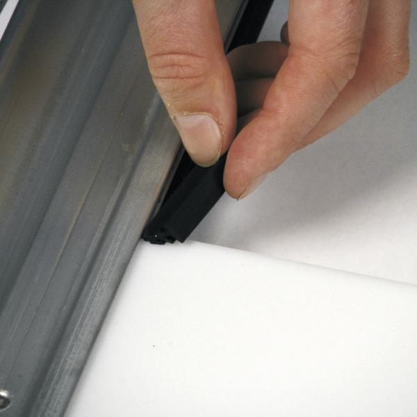 Hand setzt schwarzen Dichtungsstreifen in Metallrahmen auf weißer Oberfläche ein.