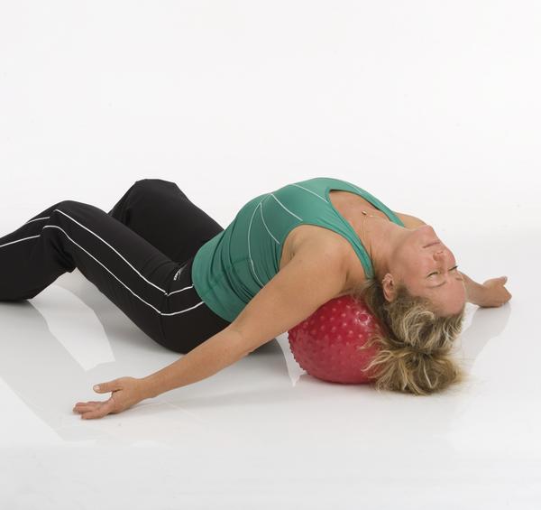 Frau entspannt auf rotem Massageball in Rückenstreckung auf weißem Boden.