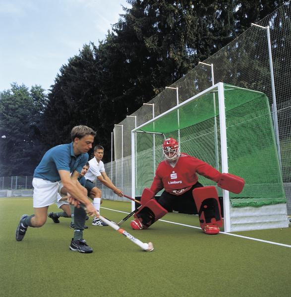 Feldhockey-Spieler beim Torschuss vor dem Torwart auf grünem Spielfeld.