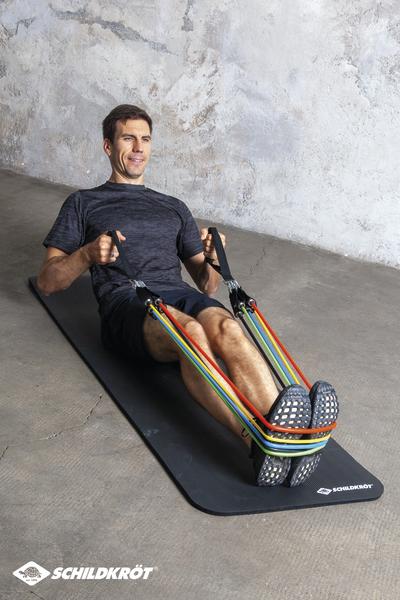 Mann trainiert mit Widerstandsbändern auf Fitnessmatte vor grauer Wand.