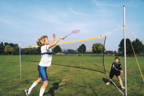 Kinder spielen Badminton im Freien auf einer grünen Wiese bei klarem Himmel.