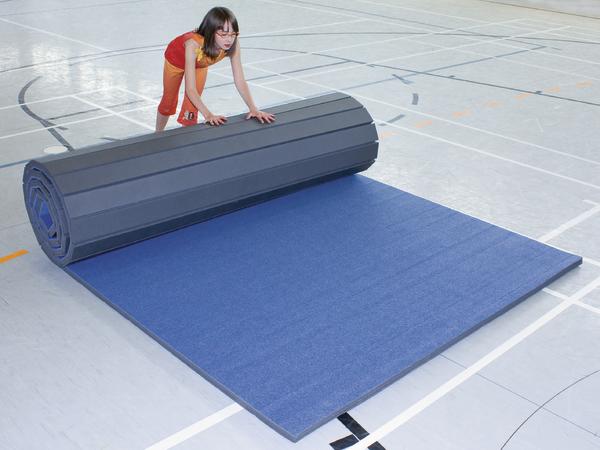 Kind rollt blauen Turnmattenboden in Sporthalle aus, Sportmatte für Gymnastik.