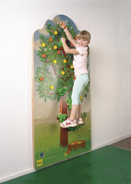 Kind klettert an einer bunten Kletterwand mit Baum- und Obstmotiv in Innenraum.
