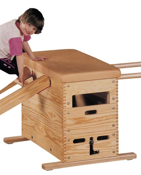 Kind klettert auf hölzernen Turnkasten mit gepolsterter Oberfläche im Sportraum