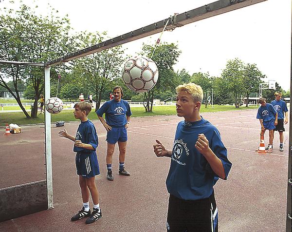 Junge Fußballspieler trainieren Ballkontrolle auf einem Outdoor-Sportplatz bei Tageslicht.