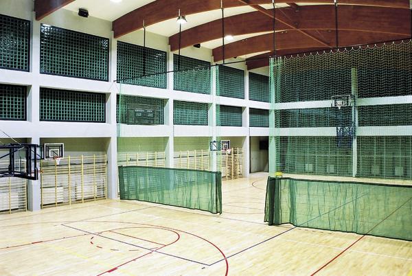 Leere Sporthalle mit Basketballkörben und grünen Trennnetzen auf hellem Holzboden.