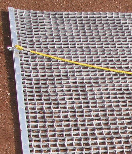 Metallgitter mit gelbem Seil auf rotem Boden, Nahaufnahme eines Bauzauns.