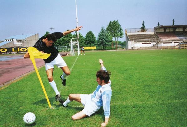 Zwei Fußballspieler kämpfen um den Ball an der Eckfahne auf einem grünen Spielfeld.