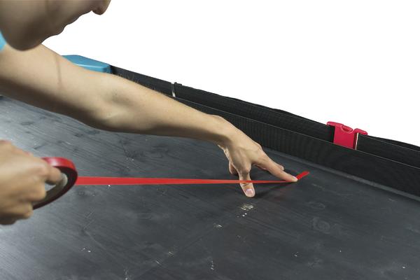 Person bringt roten Klebestreifen auf schwarzer Oberfläche mit Klebebandspender an.