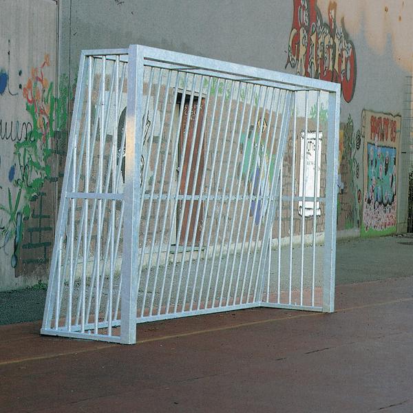 Weißes Metall-Fußballtor auf einem urbanen Sportplatz mit Graffiti an der Wand.