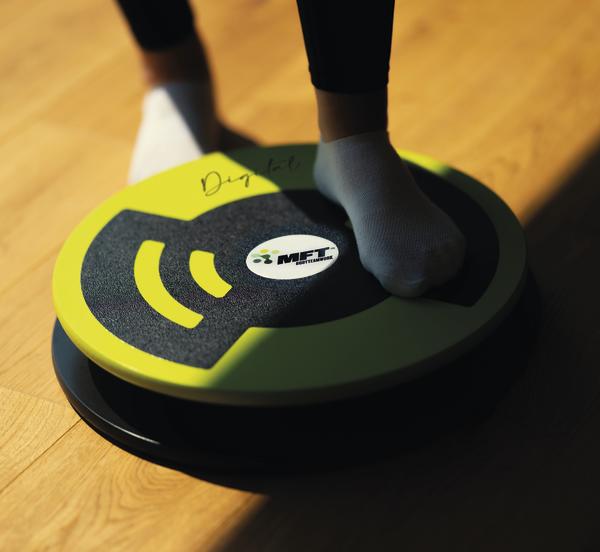 Füße auf grün-schwarzem Balance-Board auf Holzboden für Gleichgewichtstraining.