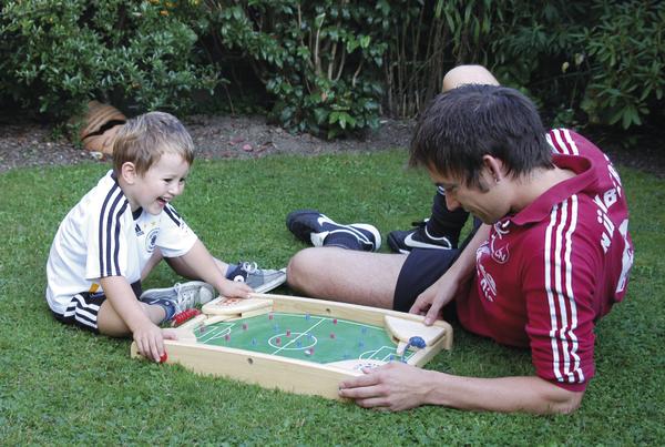 Junge und Mann spielen Tischfußball im Garten auf grünem Rasen.