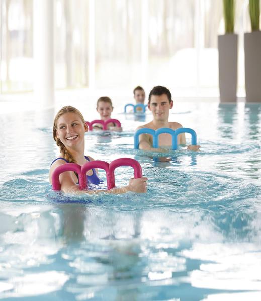 Menschen machen Wassergymnastik im Hallenbad mit bunten Schwimmhilfen.
