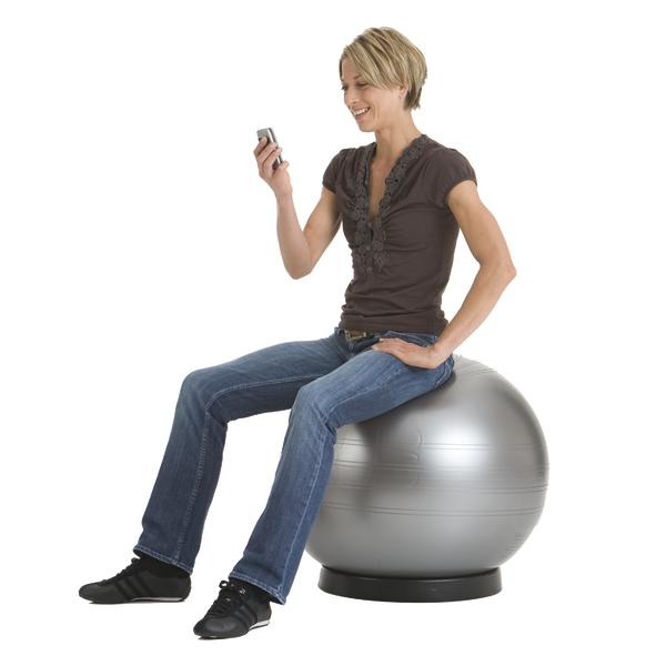 Frau sitzt auf Gymnastikball und nutzt Smartphone, lächelnd, weißer Hintergrund.