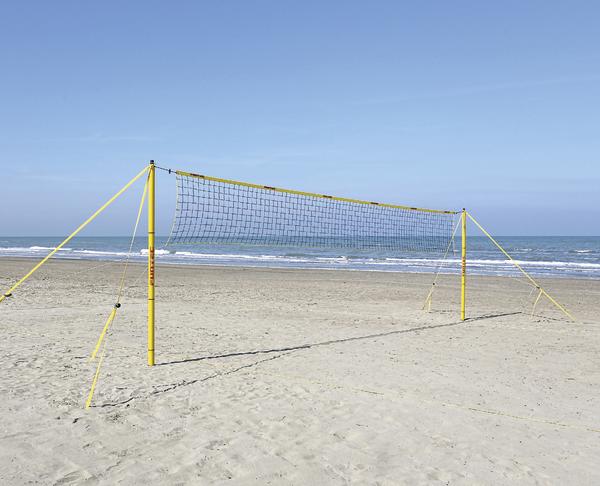 Leeres Beachvolleyballnetz am Sandstrand mit Meer und blauem Himmel im Hintergrund.