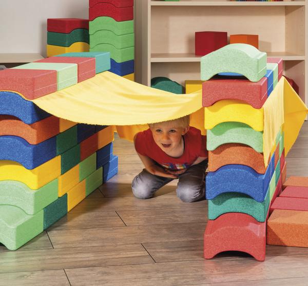 Kleiner Junge kriecht durch eine aus bunten Schaumstoffbausteinen gebaute Spielhöhle.