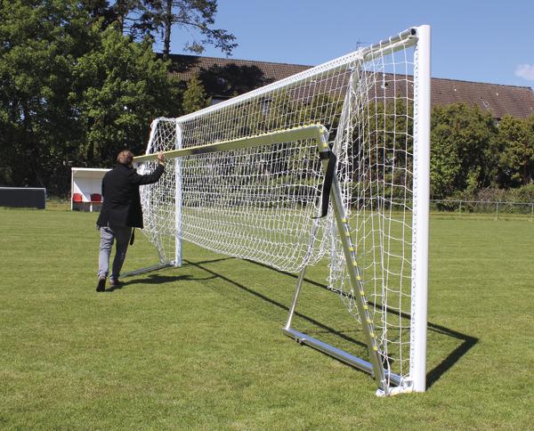 Mann faltet mobiles Fußballtor auf grünem Spielfeld bei sonnigem Wetter.