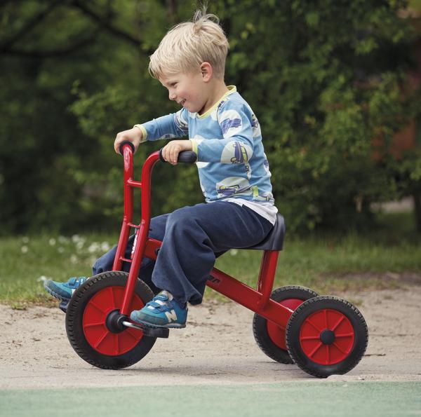 Kleiner Junge fährt fröhlich rotes Dreirad im Park bei Sonnenschein.
