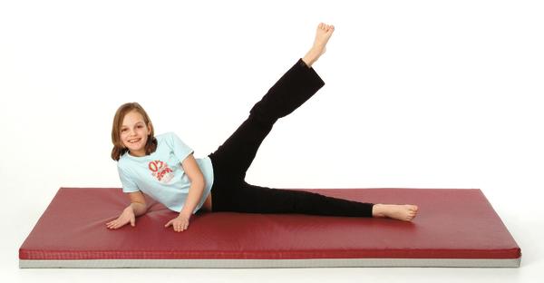Mädchen macht Beinheben auf roter Gymnastikmatte vor weißem Hintergrund.