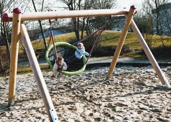 Kinder spielen auf einer grünen Nestschaukel im Sand auf einem Spielplatz im Freien.