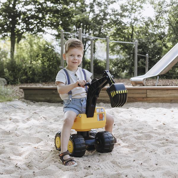 Kind spielt mit gelbem Bagger-Spielzeug im Sandkasten auf dem Spielplatz bei Sonnenschein.