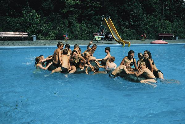 Kinder spielen und toben gemeinsam im Schwimmbecken an einem sonnigen Tag.