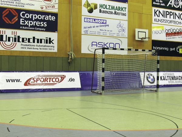 Handballtor in einer Sporthalle mit Werbebannern an der Wand und Basketballkorb.