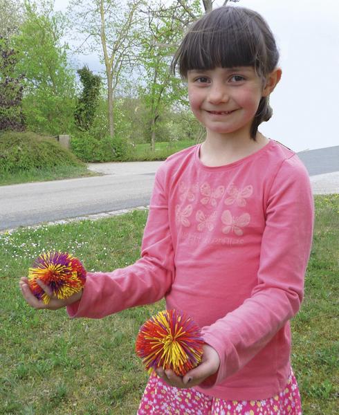 Mädchen im rosa Shirt hält bunte Spielbälle im Garten an einem Frühlingstag.