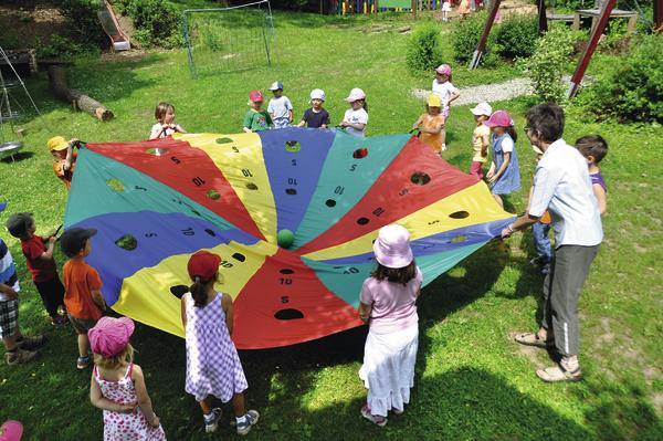Kinder spielen mit einem bunten Schwungtuch im Freien auf einer grünen Wiese.