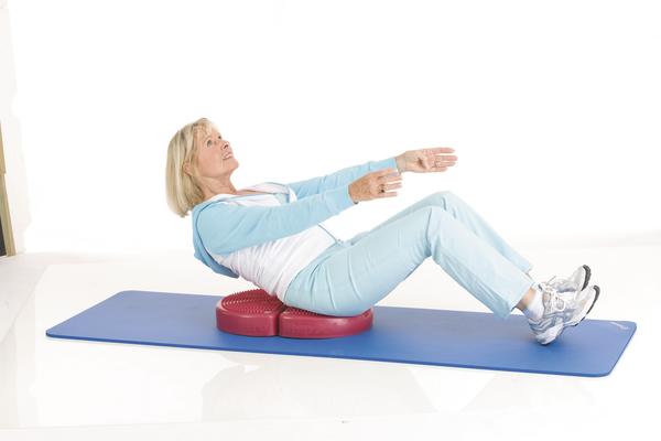 Frau macht Rückenübungen auf Balancekissen auf blauer Gymnastikmatte.