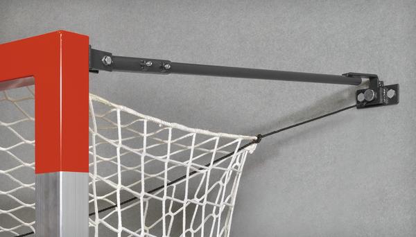 Handballtor mit rotem Pfosten, weißem Netz und schwarzem Spannarm an grauer Wand.