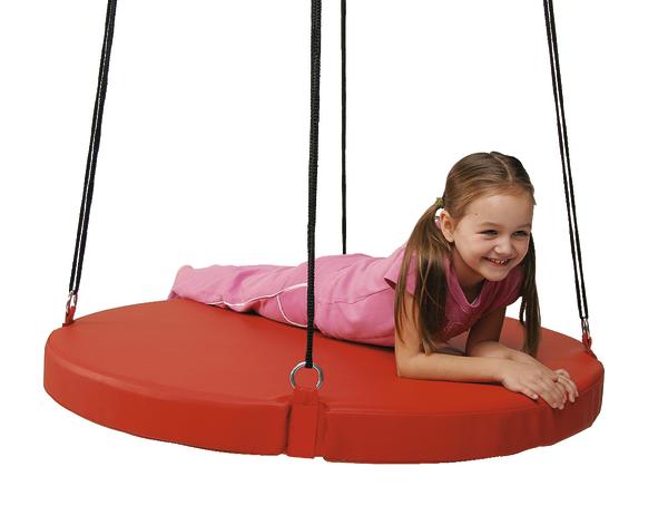 Mädchen liegt lachend auf roter runder Nestschaukel mit schwarzen Seilen vor weißem Hintergrund.
