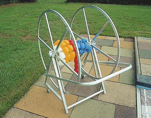 Metallischer Haspelwagen auf gepflastertem Boden neben Rasen.