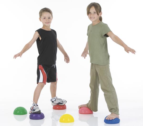 Zwei Kinder balancieren auf bunten Igelbällen, üben Koordination und Gleichgewicht.