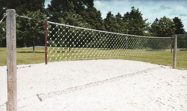 Beachvolleyballfeld mit Netz auf Sandplatz und Bäumen im Hintergrund bei klarem Himmel.