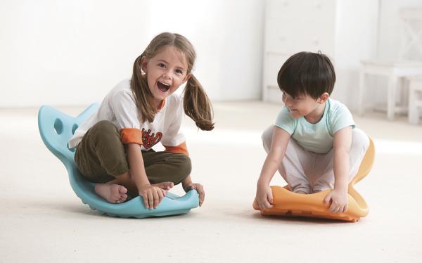 Kindermädchen und Junge spielen lachend auf bunten Sitzschaukeln im hellen Raum.