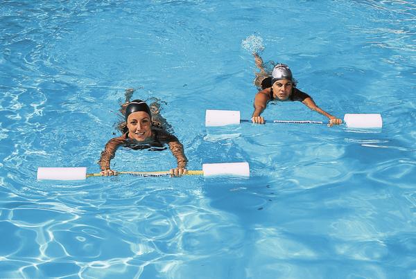 Zwei Frauen trainieren Aquafitness mit Schwimmstangen im klaren Schwimmbadwasser.